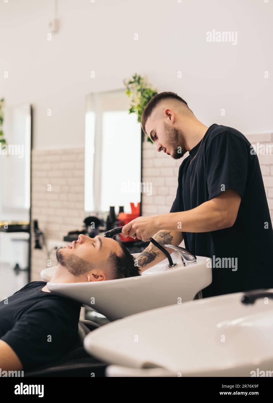 Vista lateral del joven barbero que lava el pelo del hombre de los ojos  cerrados en la peluquería contra el fondo burred Fotografía de stock - Alamy
