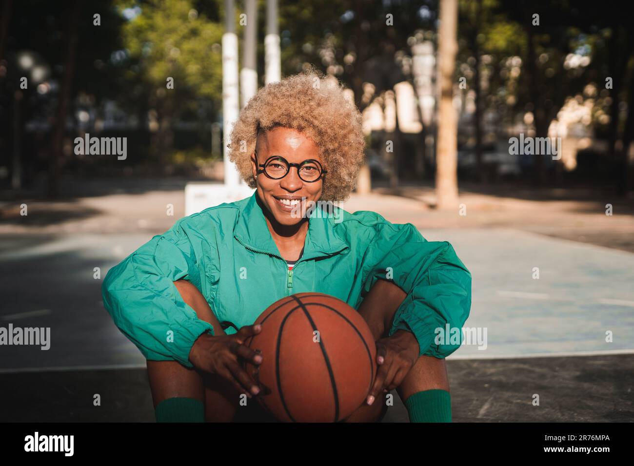 Mujer joven sentada en la cancha de baloncesto fotografías e