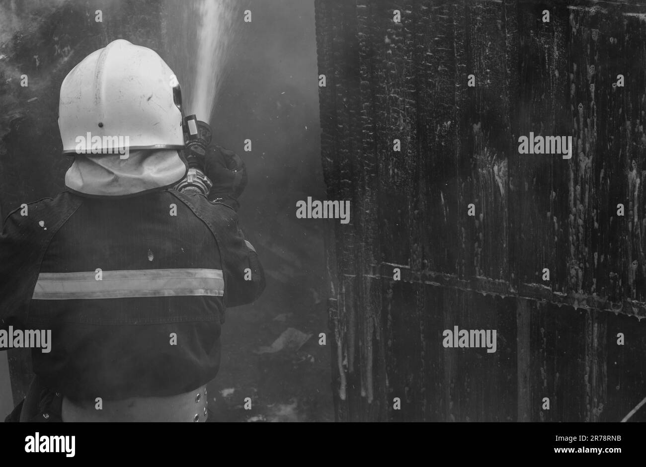 Bombero - hombres de trabajo. Bombero rociando agua a alta presión al fuego. Entrenamiento de bomberos con llamas peligrosas. Fuerte valiente bombero usando Foto de stock