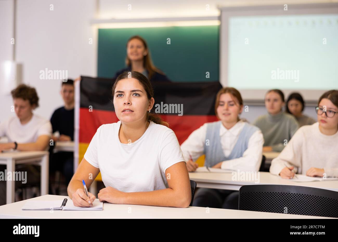 La maestra de secundaria tiene la bandera de Alemania en sus manos y habla de este país en la lección de geografía Foto de stock