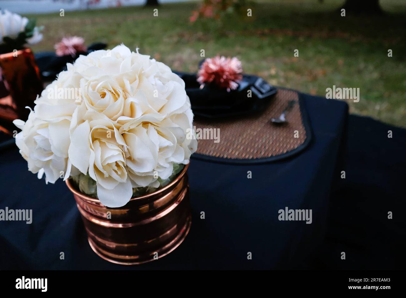 Un jarrón de cobre lleno de flores blancas en una mesa negra en el patio Foto de stock
