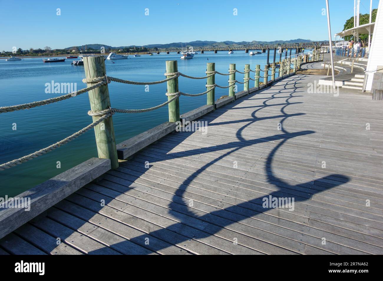 Patrones de sombra de bolardos de cuerda y poste a lo largo de la costa de la ciudad de Tauranga. Con puerto y fondo de cielo azul. Foto de stock