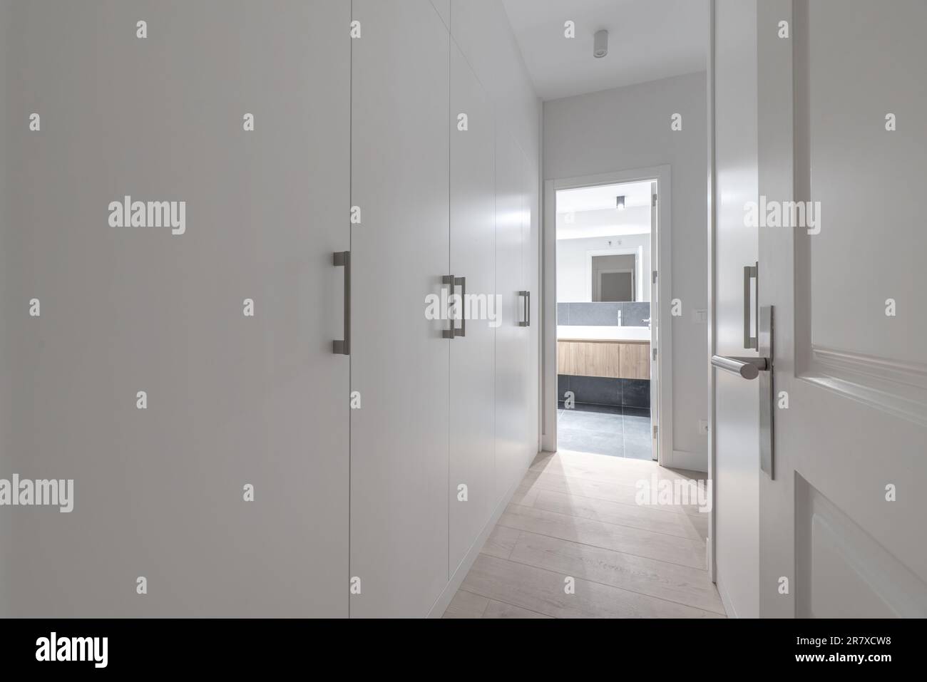 Dormitorio en el pasillo con gabinetes de madera blanca, pisos de madera y acceso a un baño en suite Foto de stock