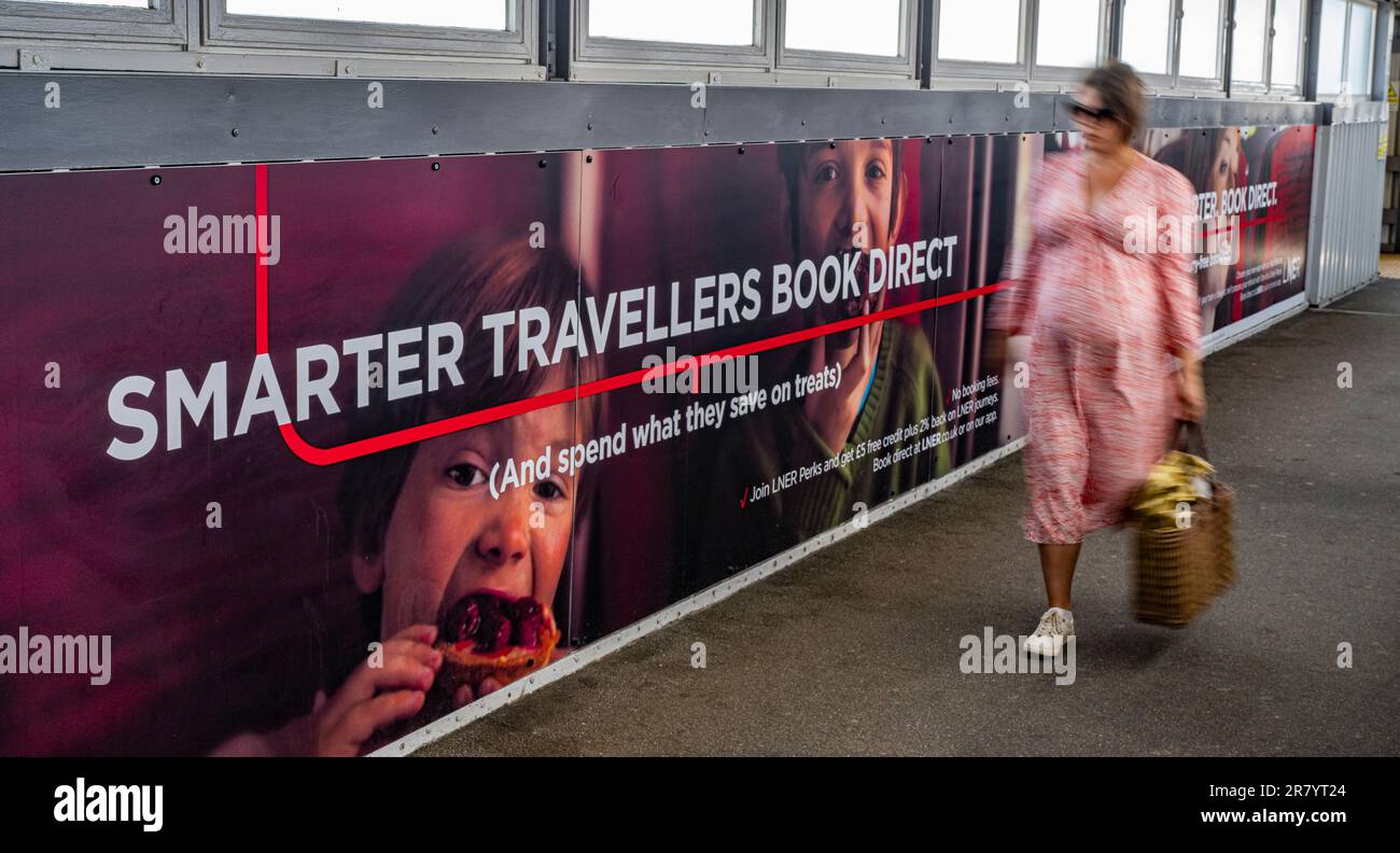 Una mujer joven que pasa por un acaparamiento de publicidad para el ferrocarril del noreste de Londres (LNER) para viajes más inteligentes y reservar directamente Foto de stock