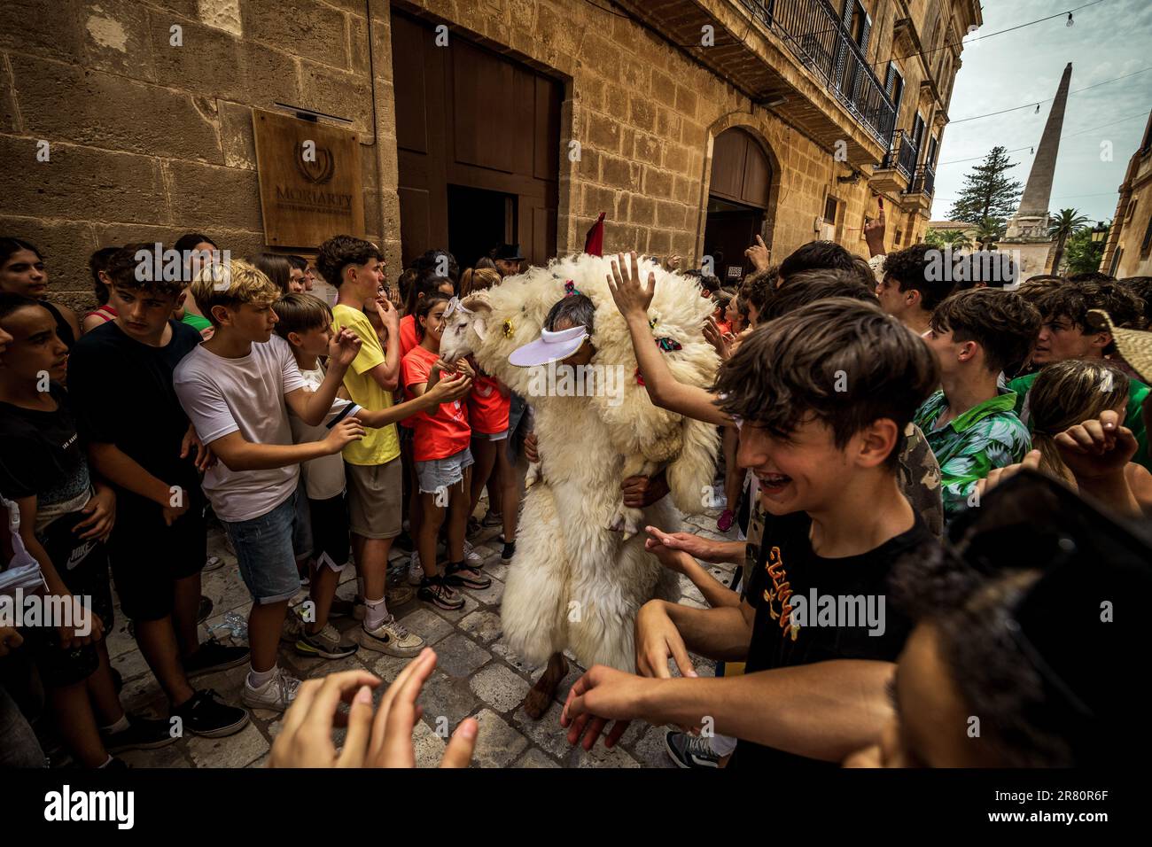 Ciutadella, España. 18 de junio de 2023. Un joven vestido de piel de oveja,  el 'Homo des Be' (hombre de ovejas), lleva un carnero vivo alrededor de sus  hombros mientras pasa el