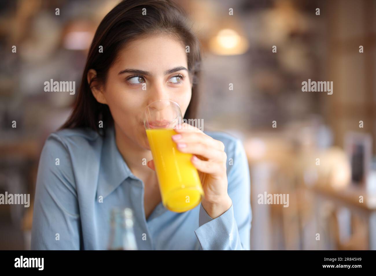 Mujer distraída mirando lado bebiendo jugo de naranja en un interior de bar Foto de stock