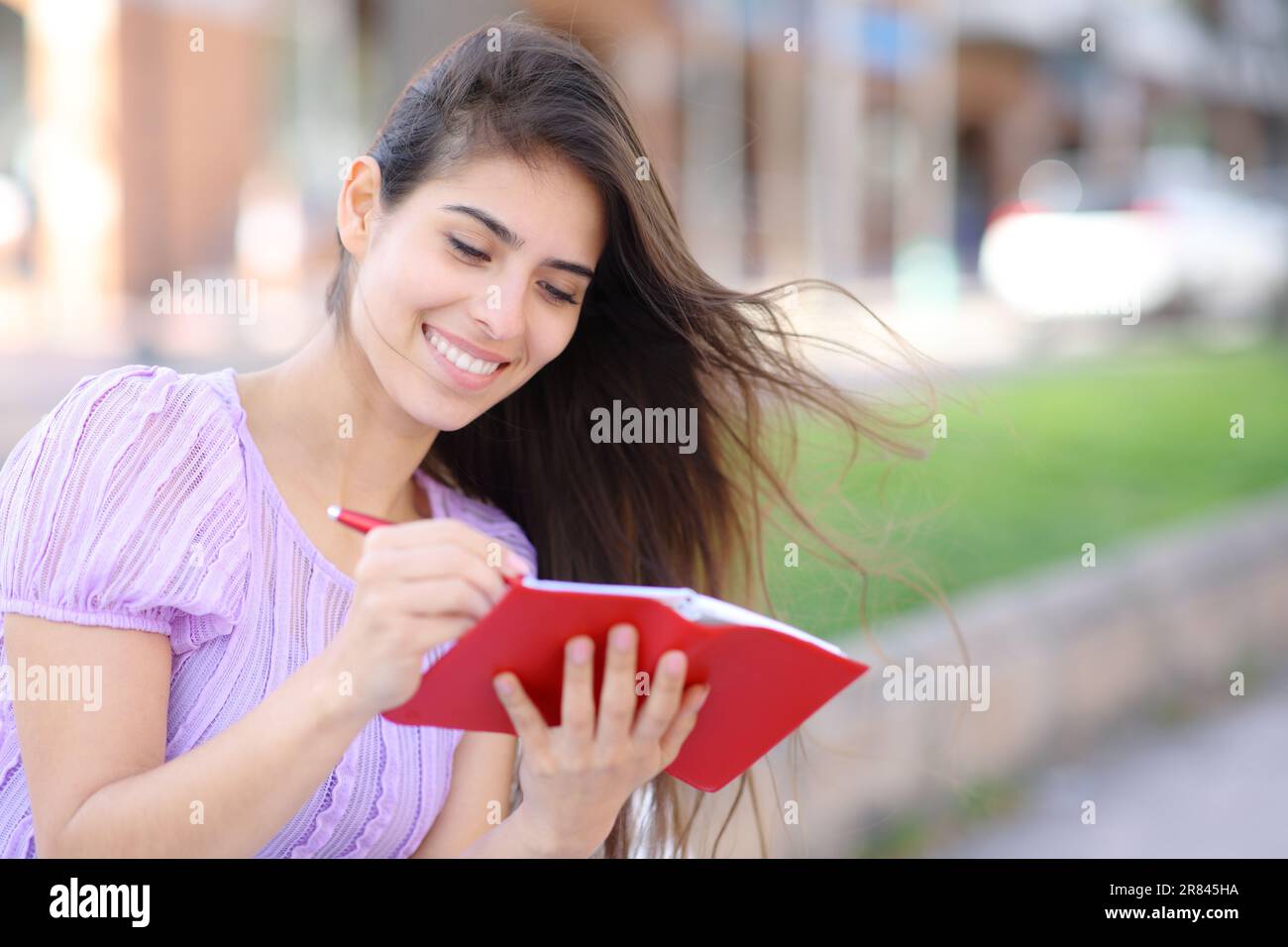 Mujer feliz que escribe en la agenda roja usando la pluma en la calle Foto de stock