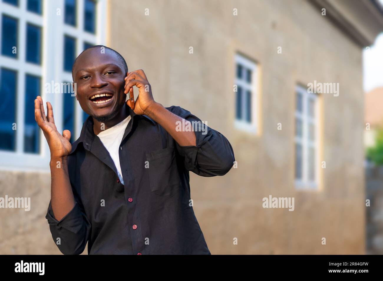 hombre negro emocionado en camisa negra usando su teléfono móvil. haciendo uso de la tecnología inalámbrica Foto de stock