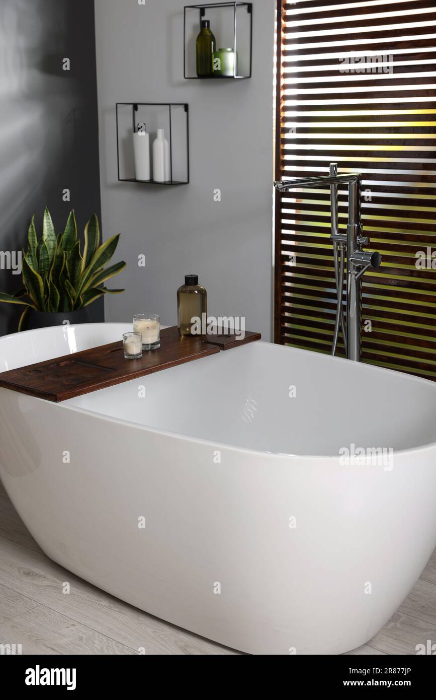Elegante interior del baño con bañera de cerámica, velas y productos de  cuidado en la bandeja de baño de madera Fotografía de stock - Alamy