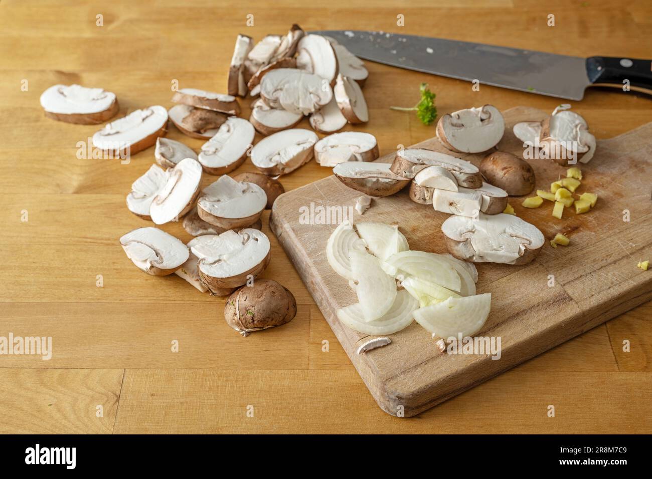Rodajas de champiñones, cebolla, jengibre picado y un cuchillo de cocina en una tabla de cortar de madera, cocinar un plato vegetariano saludable, espacio de copia, focu seleccionado Foto de stock