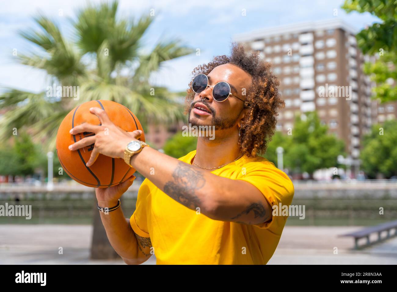 Retrato de un hombre afro-haired en una camiseta amarilla con una pelota de baloncesto. retrato en la ciudad Foto de stock