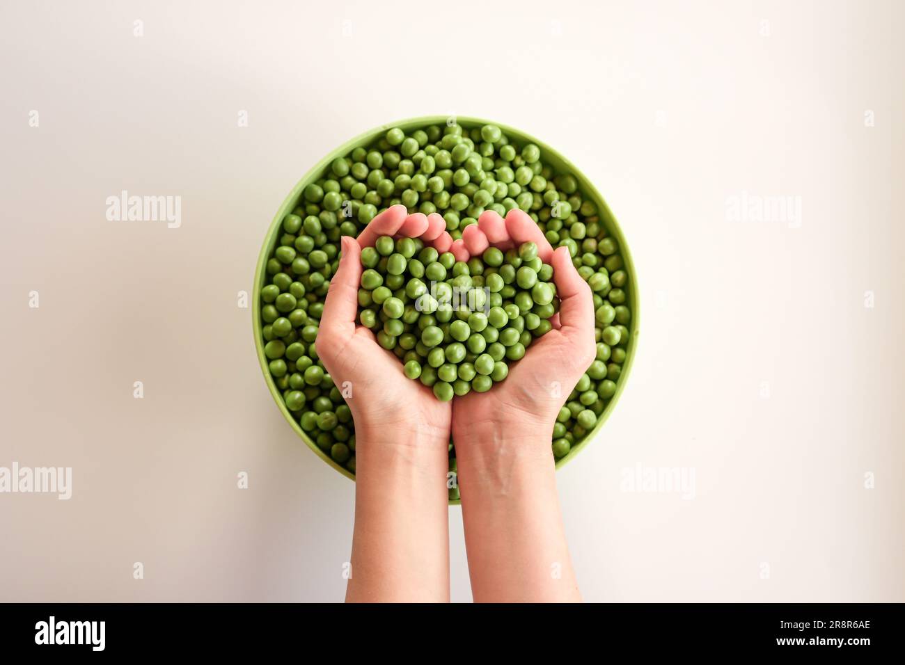 Primer plano de muchos guisantes maduros en las manos, en forma de corazón. Guisante verde en un tazón verde. Comida sabrosa y saludable. Verduras Foto de stock