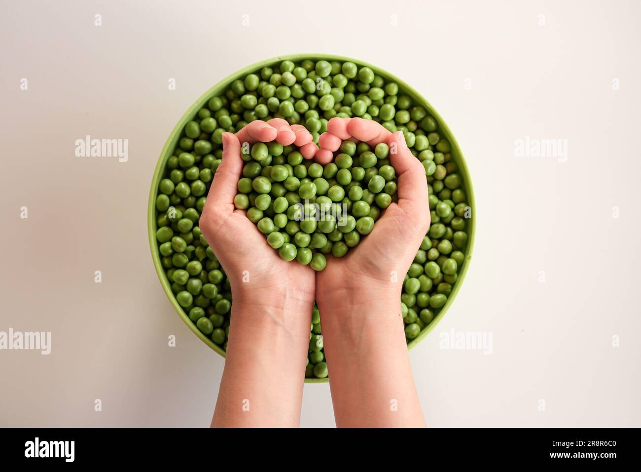 Primer plano de muchos guisantes maduros en las manos, en forma de corazón. Guisante verde en un tazón verde. Comida sabrosa y saludable. Verduras Foto de stock