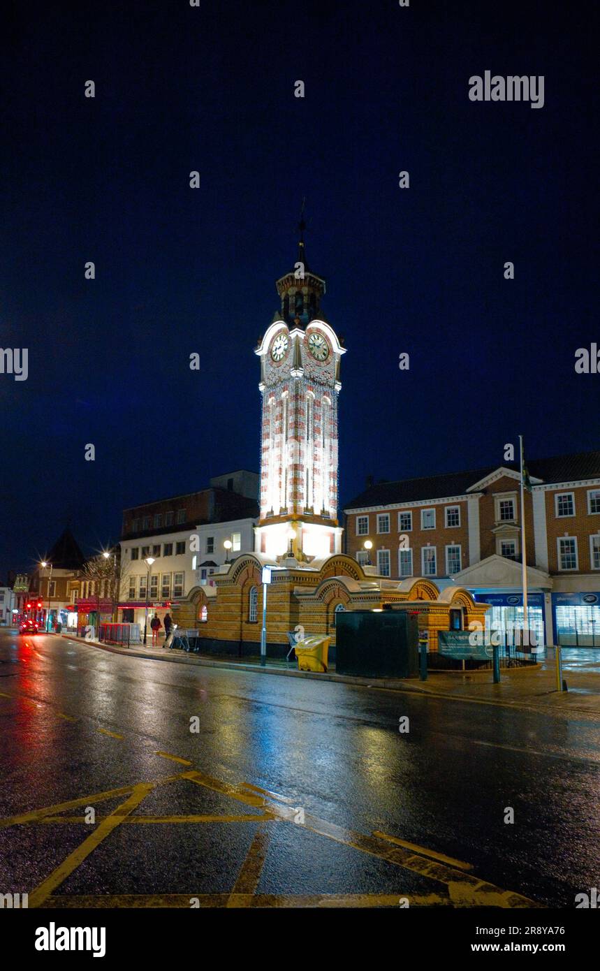 La torre central del reloj en Epsom se iluminó por la noche en una noche húmeda Foto de stock