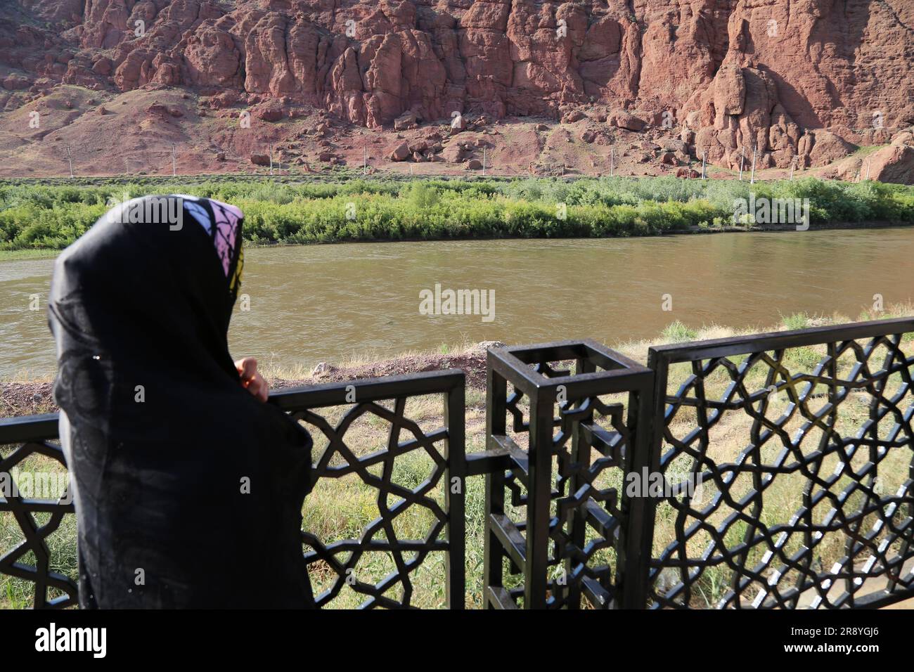 21 de junio de 2023, Jolfa, Azerbaiyán Oriental, Irán: Una mujer velada en un chador negro mira el río Aras en la frontera entre el noroeste de Irán y Azerbaiyán. El Aras (los Araks, Arax, Araxes, o Araz) es un río en el Cáucaso. Se levanta en el este de Turquía y fluye a lo largo de las fronteras entre Turquía y Armenia, entre Turquía y el exclave de Najicheván de Azerbaiyán, entre Irán y Azerbaiyán y Armenia, y, finalmente, a través de Azerbaiyán, donde desemboca en el río Kura. Drena el lado sur de las montañas del Cáucaso Menor, mientras que el Kura drena el lado norte de las caucas menores Foto de stock