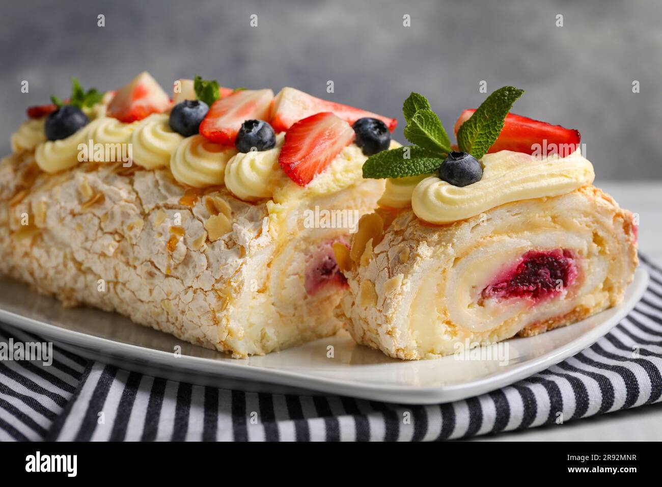 Sabroso rollo de merengue con mermelada, crema, fresa, arándanos y menta en el plato, primer plano Foto de stock