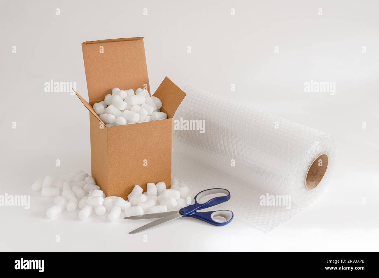 Caja de cartón aislada en el fondo blanco lleno de cacahuetes de embalaje más plástico de burbujas y tijeras Foto de stock