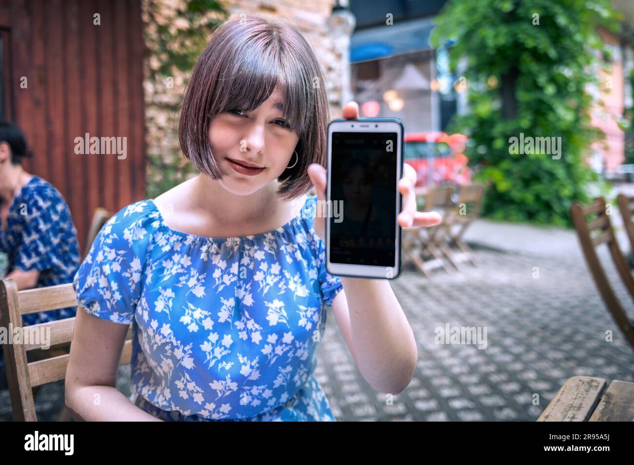 Adolescente con el teléfono móvil en el café al aire libre. Hermosa chica showiing teléfono inteligente en café Foto de stock