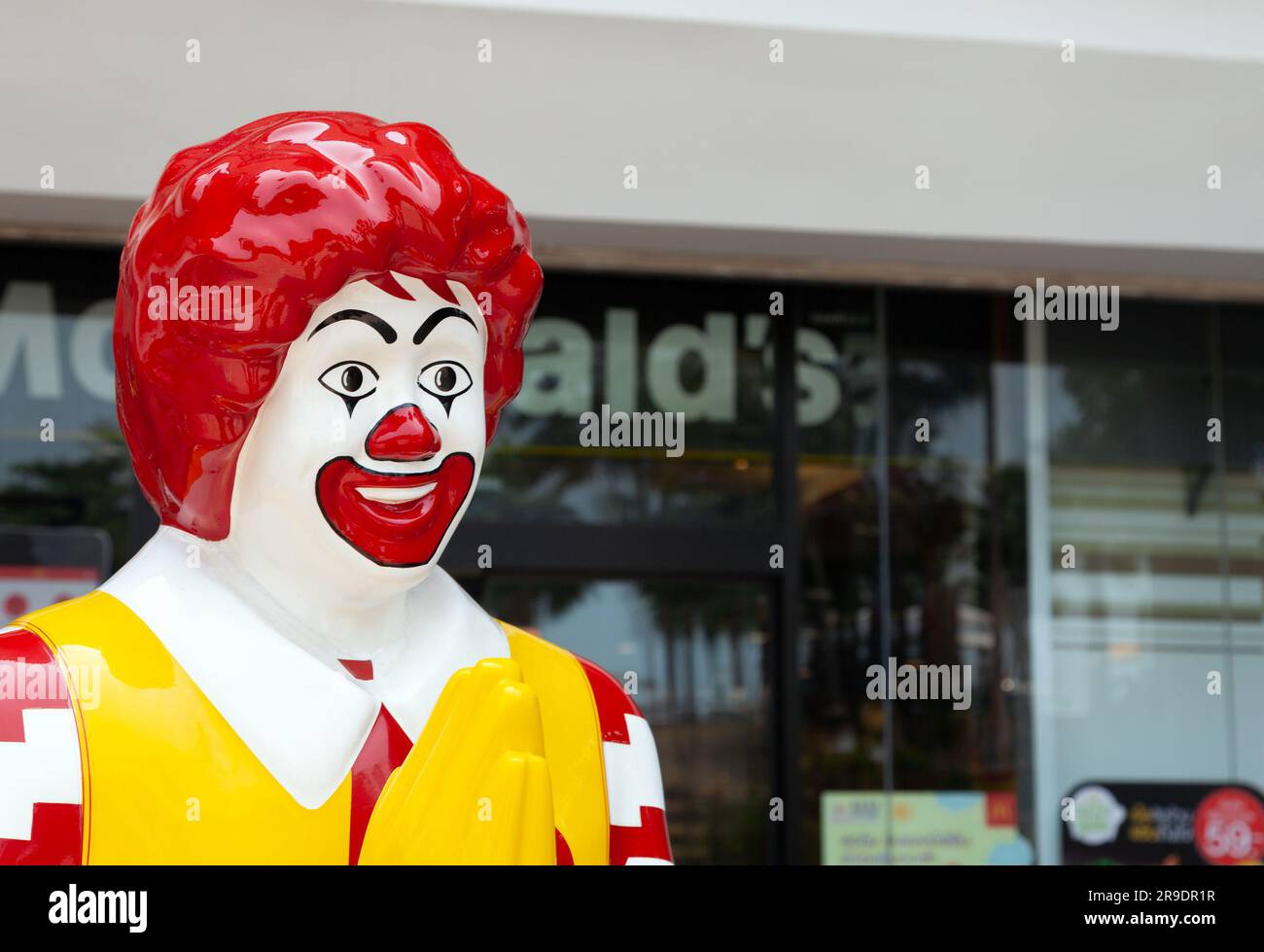Estatua de plástico de Ronald McDonald saludando a los clientes con un gesto de namaste frente al restaurante McDonalds. Cadena de comida rápida colorida mascota meeting clien Foto de stock