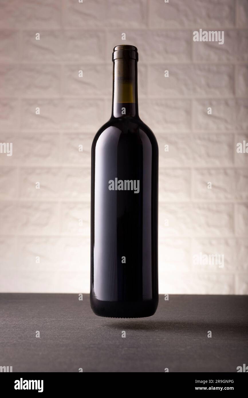 Maqueta de botella de vino tinto sin etiqueta que flota en la superficie de piedra gris, fondo de pared de ladrillo rústico blanco. Concepto minimalista. Foto de stock