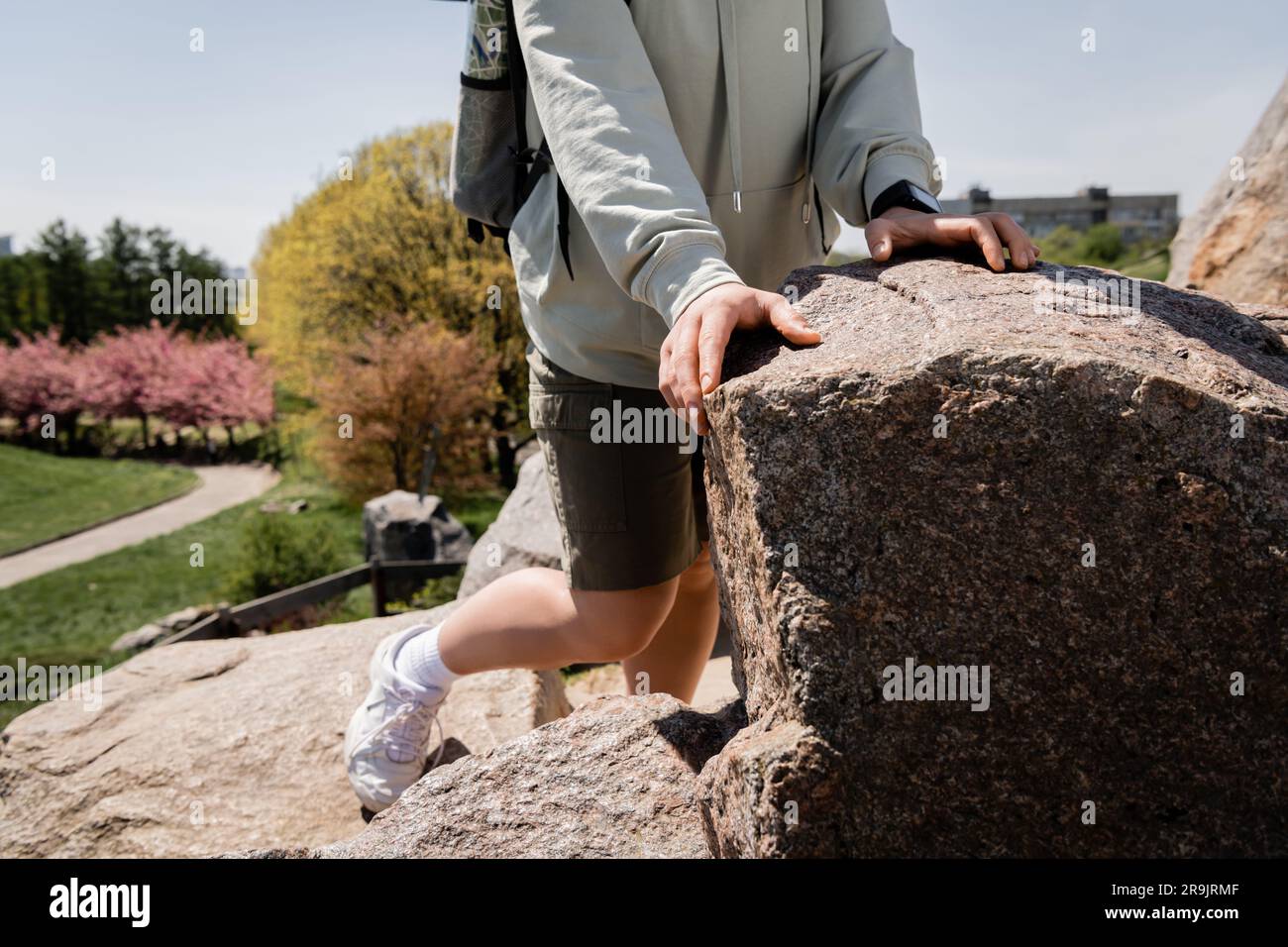 Vista recortada del excursionista femenino joven con mochila y rastreador de fitness de pie cerca de piedras en la colina con naturaleza borrosa en el fondo, viaje vibrante ex Foto de stock