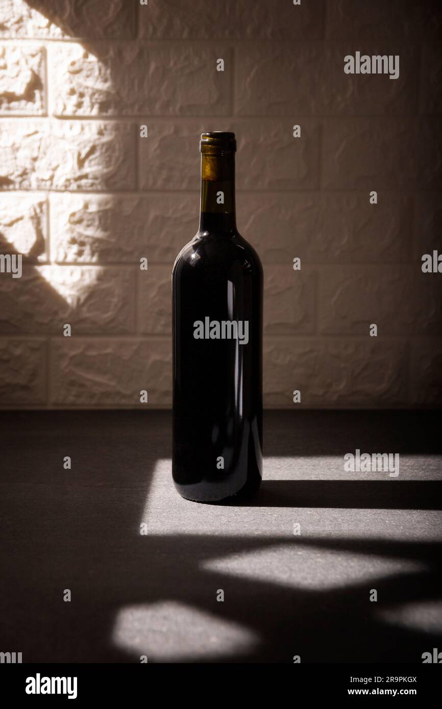 Maqueta de botella de vino tinto sin etiqueta en superficie de piedra gris, fondo de pared de ladrillo blanco texturizado. Sombras largas diagonales. Concepto minimalista. Foto de stock