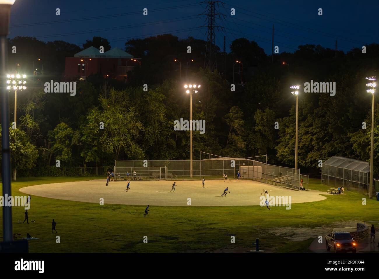 ¡Juega a la pelota! Un partido de béisbol de la liga de recreación se juega bajo las luces en un gran parque en Toronto en una buena noche de verano Foto de stock