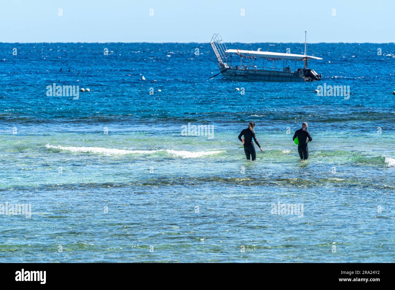 Buceadores entrando en el agua con barcos con fondo de vidrio anclados en el fondo, Lighthouse Beach, Lady Elliot Island Eco Resort, Queensland, Australia Foto de stock
