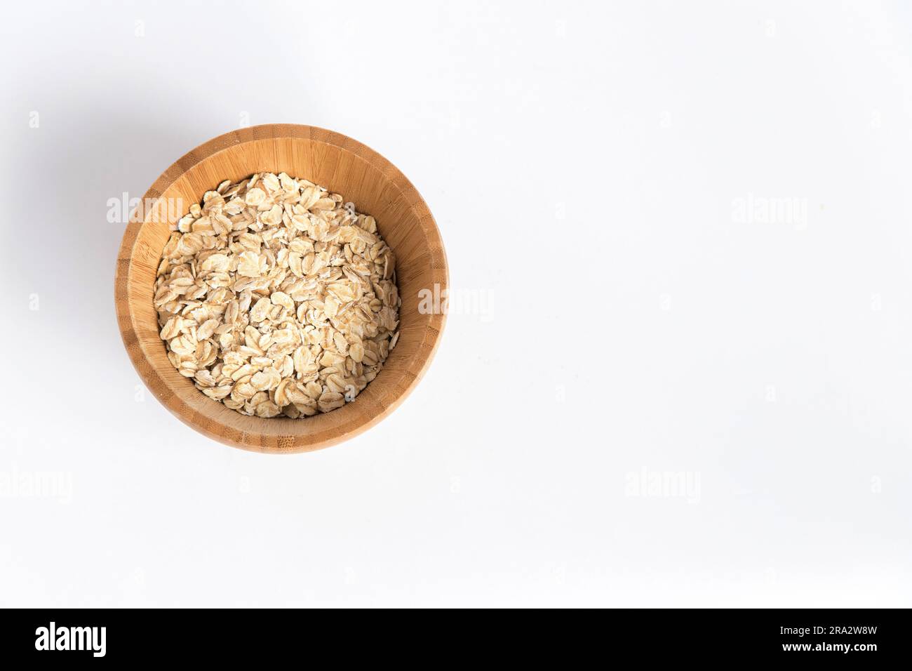 Tazón de madera lleno de copos de avena sobre fondo blanco. Súper alimento rico en nutrientes y que se puede utilizar para varias recetas. Alimentación saludable. Foto de stock