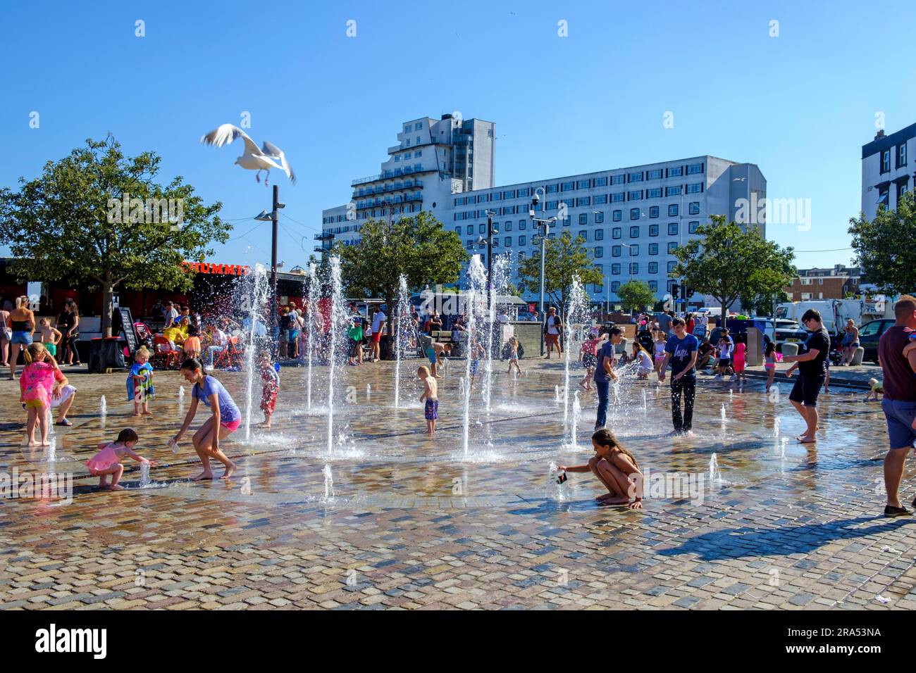 Niños jugando en la fuente en un día caluroso en Folkestone Harbour, Kent, Reino Unido Foto de stock