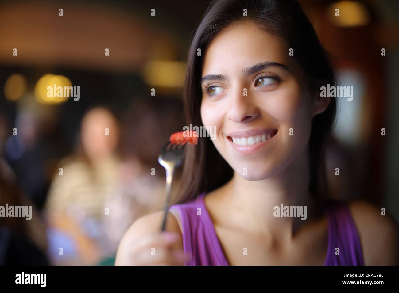 Mujer feliz comiendo fresa y mirando el lado en un restaurante Foto de stock