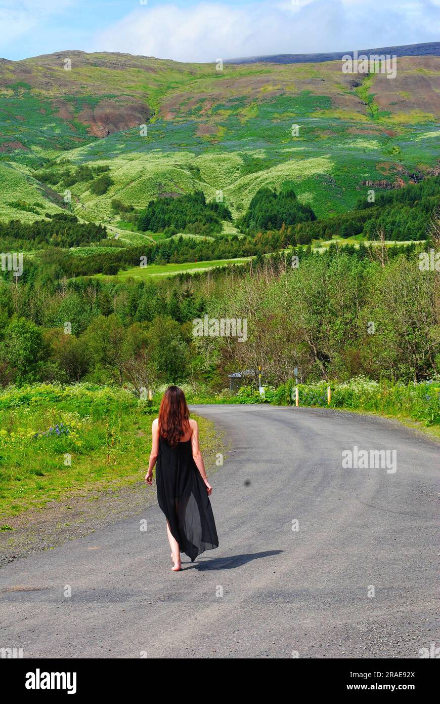 Una mujer con un vestido negro y fluido camina por un camino hacia Mt. Esja, Islandia en un día fresco de verano. Foto de stock