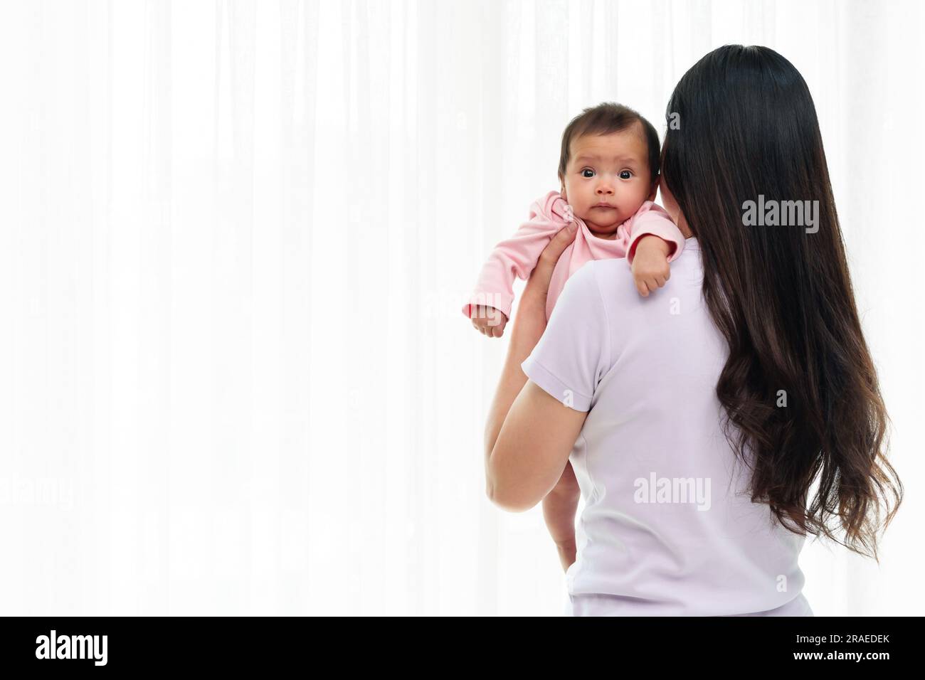 madre que sostiene al bebé recién nacido eructando después de alimentar la leche en el fondo blanco de la ventana Foto de stock