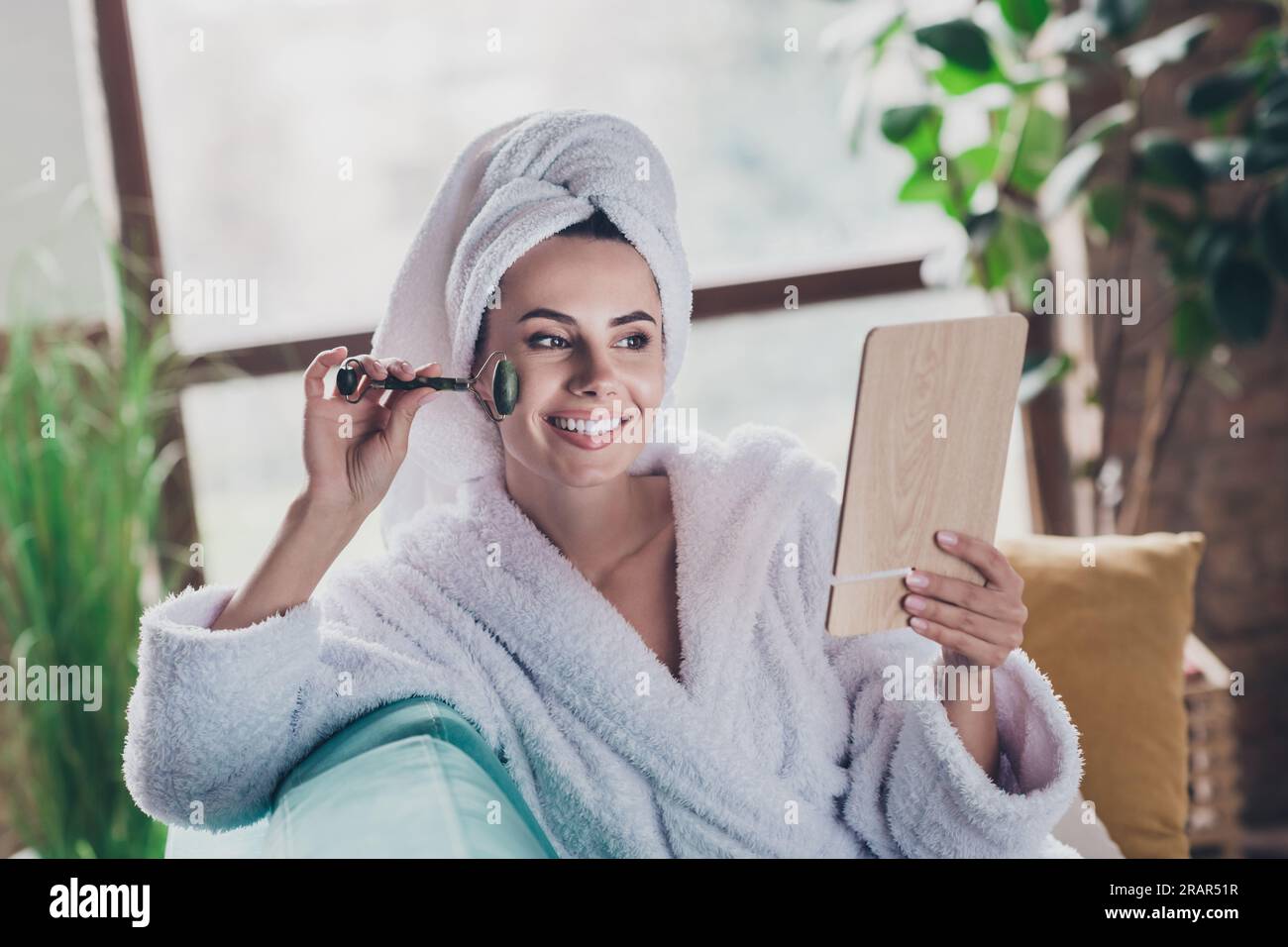 Foto de atractiva dama hogareña después de la ducha vestido albornoz  turbante de pelo haciendo cara pelando masajeador de cuarzo mirar espejo en  el interior Fotografía de stock - Alamy