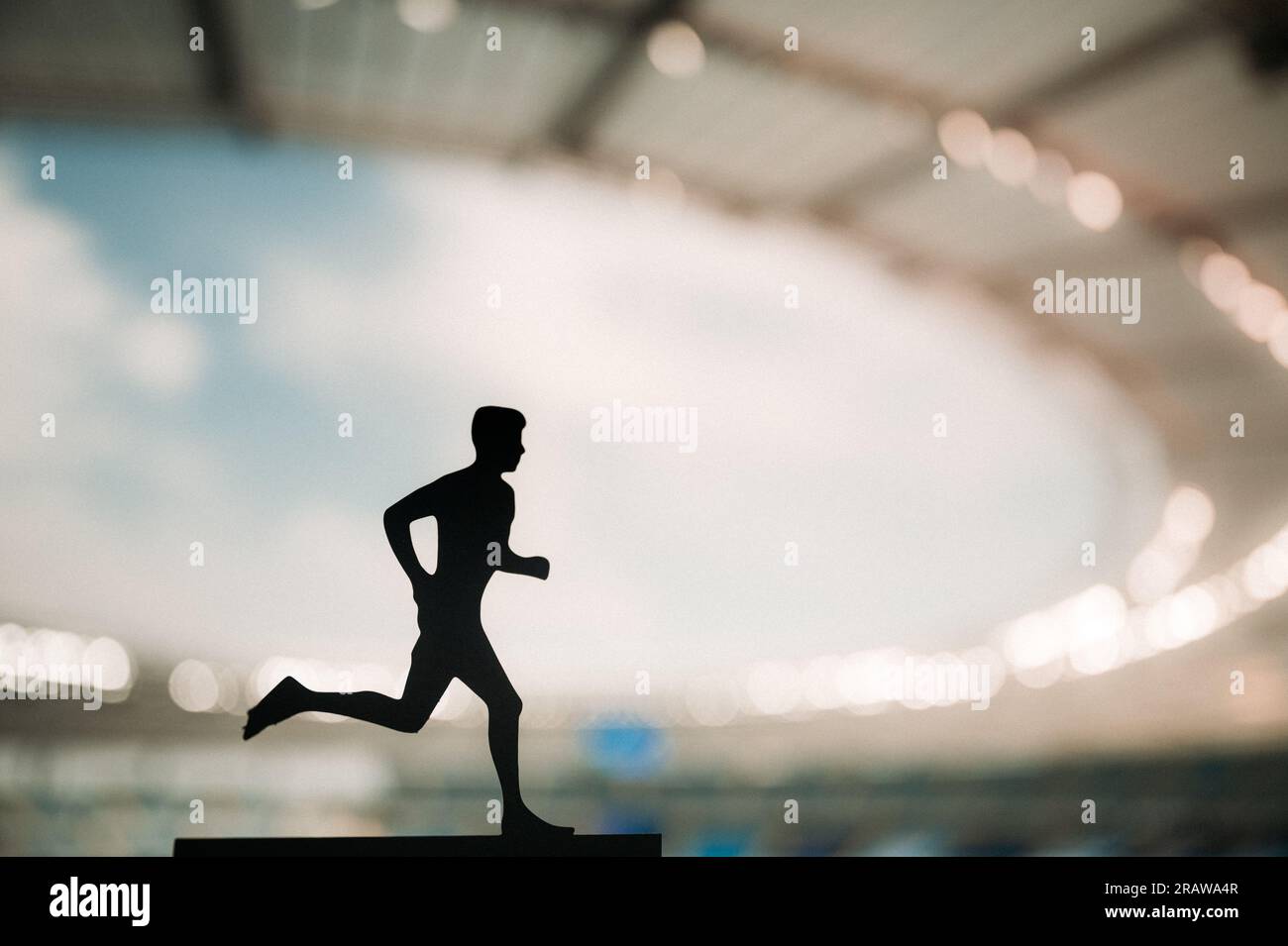 Silueta de un atleta masculino, un corredor de resistencia, prosperando bajo la encantadora luz de la tarde de un estadio deportivo moderno Foto de stock