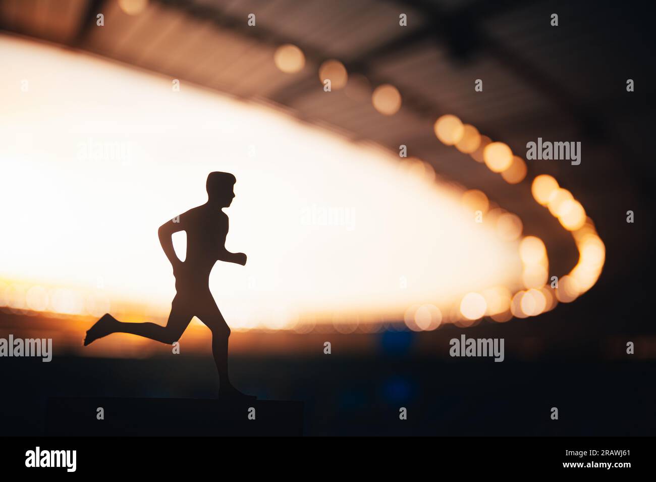 Silueta de un atleta masculino, un corredor de larga distancia, contra el telón de fondo bellamente iluminado de un estadio deportivo moderno Foto de stock