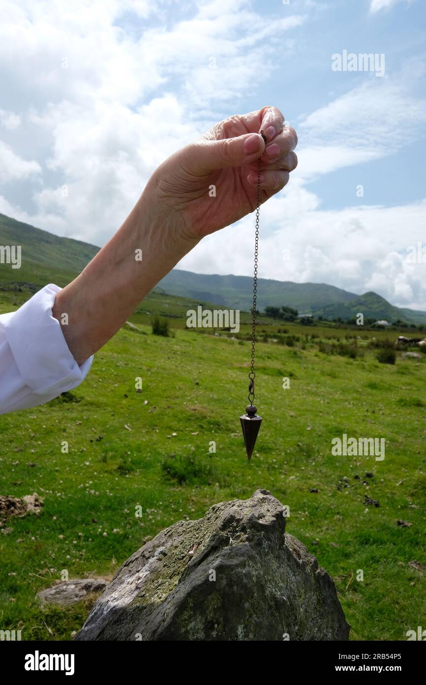 Dowser hembra sosteniendo un péndulo sobre una piedra de pie en el círculo de piedra Ardgroom, Condado de Cork, Irlanda - John Gollop Foto de stock
