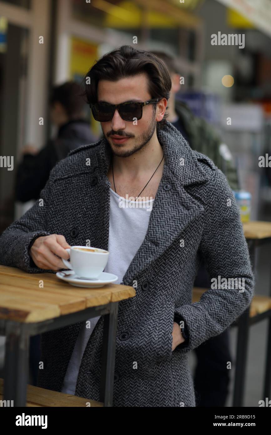 Hombre guapo con gafas de sol sentado fuera del caf bebiendo caf