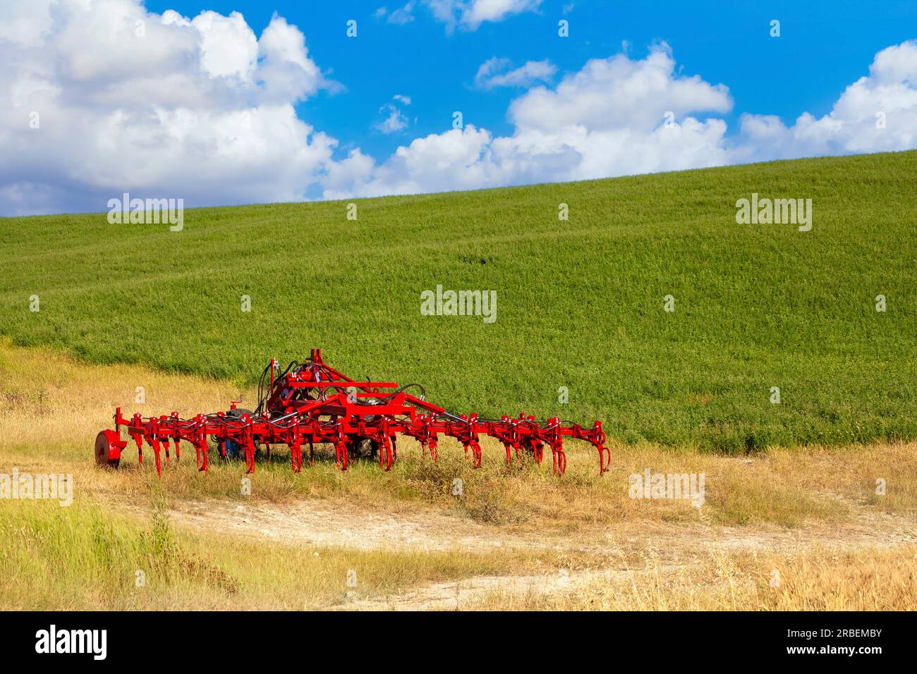 Llamativo equipo de granja roja estacionado en un pintoresco paisaje de hierba seca y exuberante pradera Foto de stock