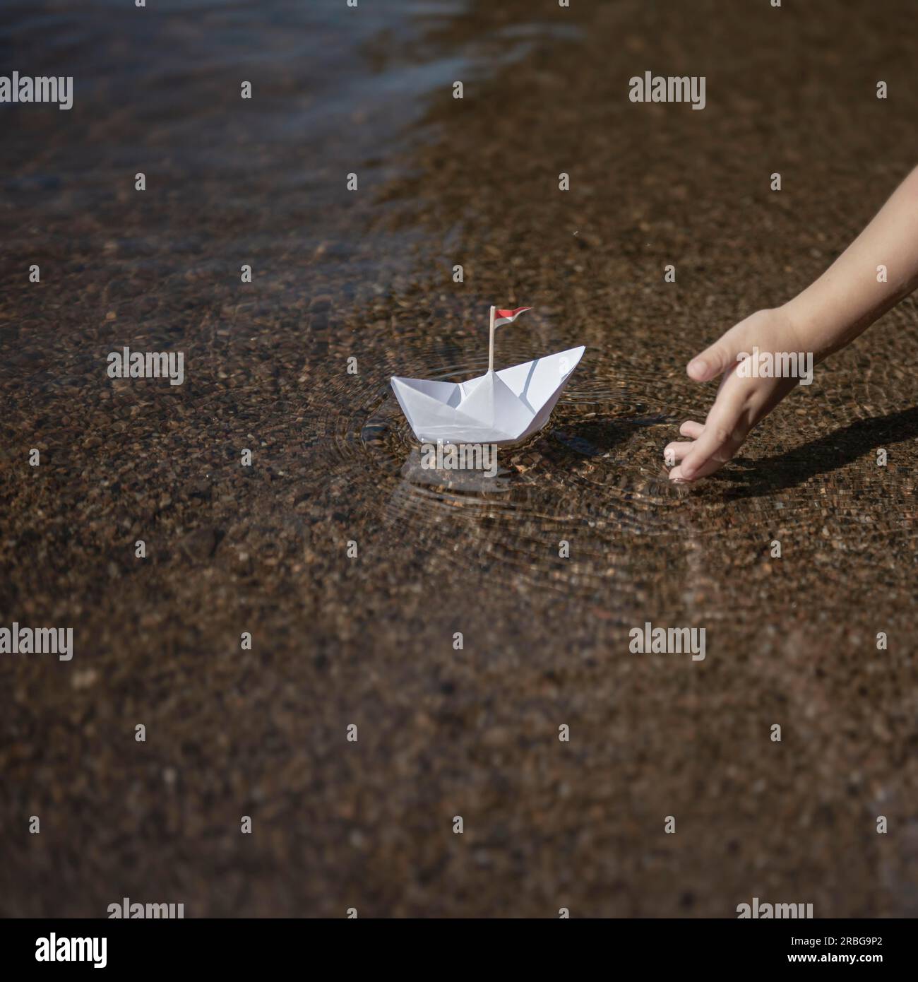 El niño pone un pequeño bote de papel en el agua Foto de stock