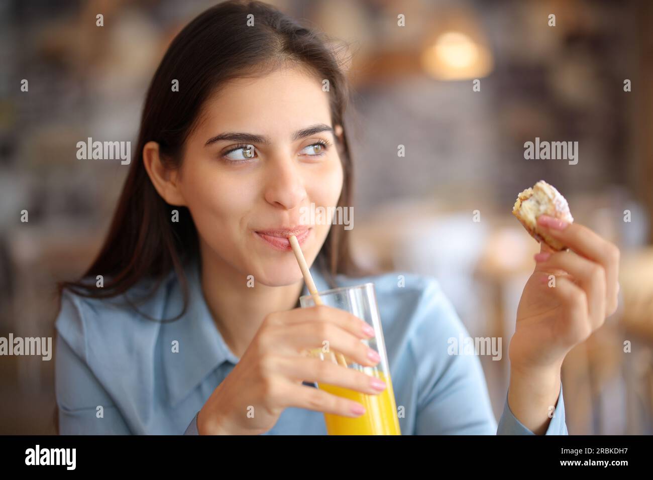 Mujer feliz bebiendo jugo comiendo croissant en un restaurante Foto de stock