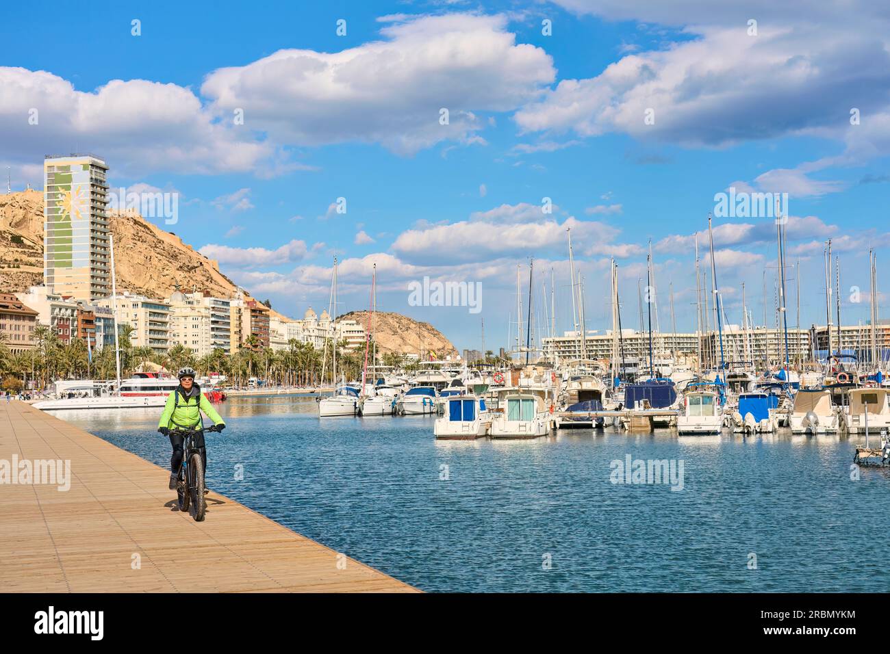 Buena mujer senior en bicicleta en un día fresco de primavera con su bicicleta eléctrica en la costa de Alicante, Costa Blanca, España Foto de stock