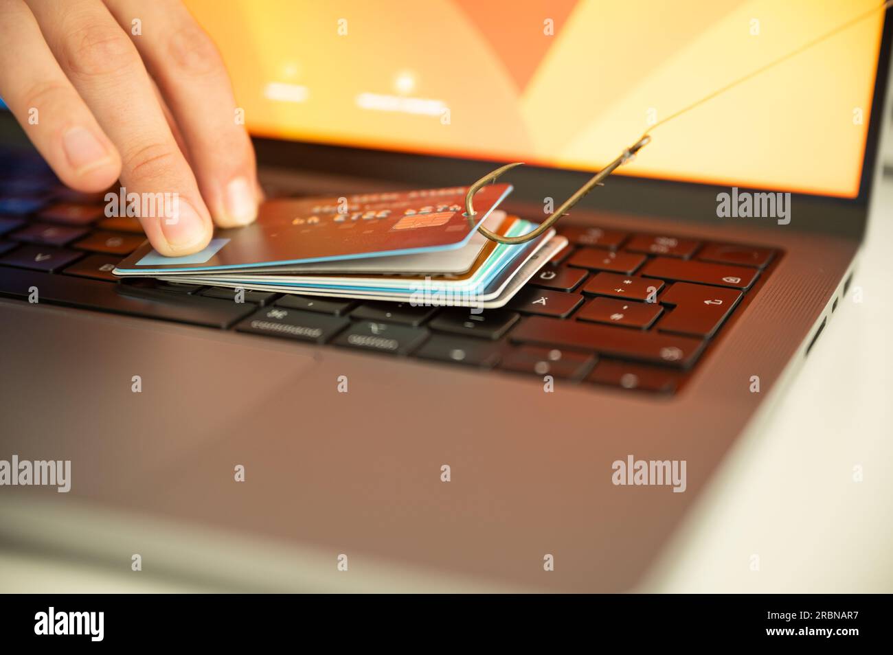 Visualización de una persona que intenta prevenir el phishing y el fraude en línea sosteniendo una tarjeta de crédito filtrada en un teclado de PC que está colgado de un gancho Foto de stock