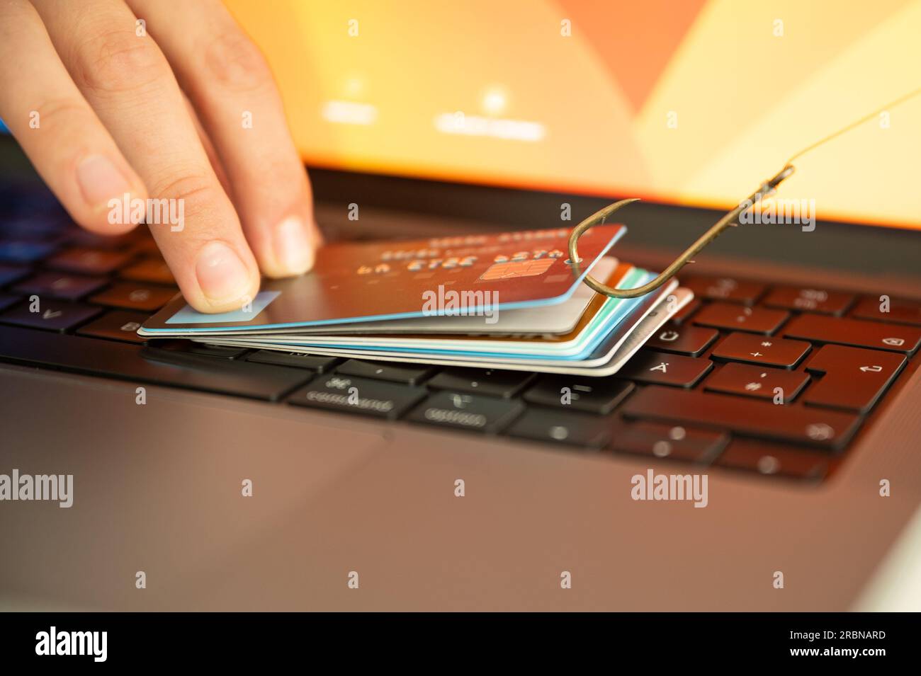 Visualización de una persona que intenta prevenir el phishing y el fraude en línea sosteniendo una tarjeta de crédito filtrada en un teclado de PC que está colgado de un gancho Foto de stock