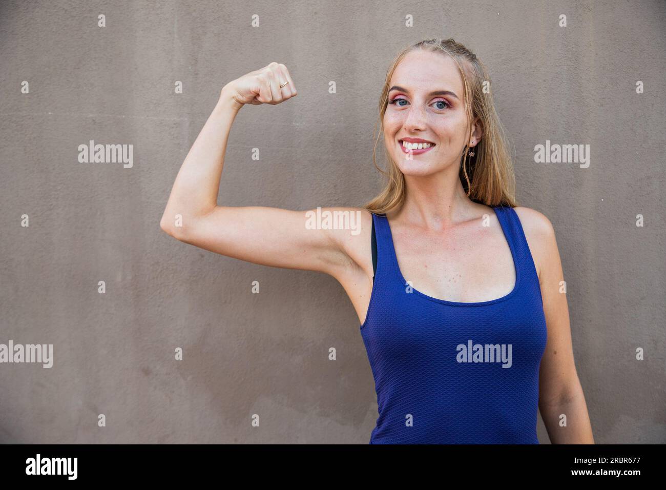 Una mujer joven con su bíceps elevado, concepto de fuerza, modelo aislado en un fondo gris Foto de stock