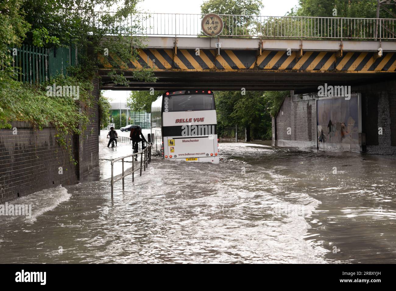 Autobús conduciendo a través de agua de inundación en la carretera durante la tormenta. Ciclista que se sujeta a las barandillas bajo el puente ferroviario. Stockport, Gran Manchester Reino Unido Foto de stock