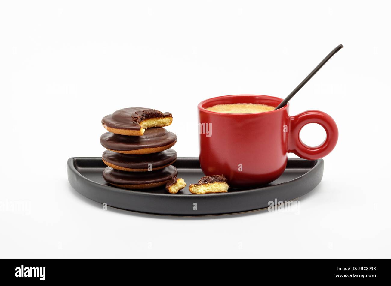Taza de café espresso rojo lleno de café fuerte y algunas galletas en plato negro aislado sobre fondo blanco Foto de stock