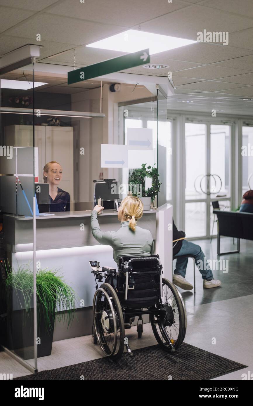 Vista posterior de la paciente femenina con discapacidad haciendo la investigación en la recepción del hospital Foto de stock