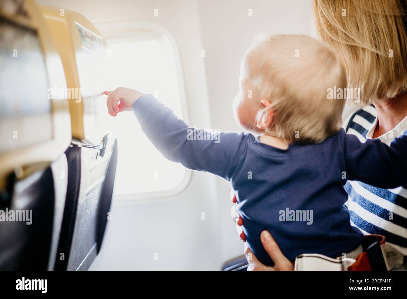 Mamá y niño volando en avión. Madre sosteniendo y jugando con su bebé niño en su regazo durante el vuelo comercial económico. Foto conceptual de Foto de stock