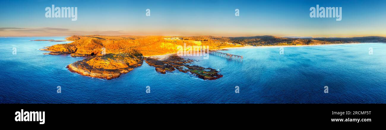 Playa de campamento medio en la costa del Pacífico de Australia en la bahía de Catherine Hill con embarcadero histórico - amplio panorama aéreo del amanecer. Foto de stock